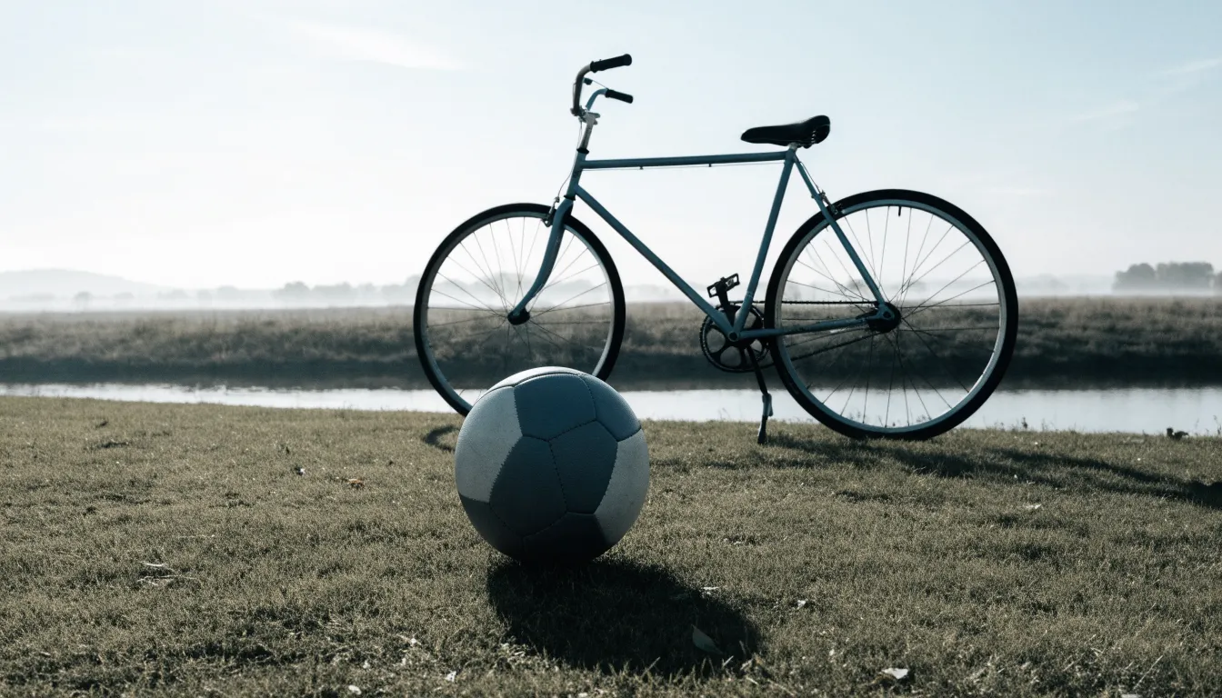 Ein Fussball liegt auf einer Wiese neben einem Fahrrad, im Hintergrund ein Kanal im Morgenlicht