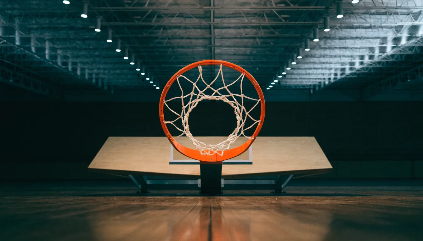 Ein Basketballkorb von unten gesehen, darüber eine Hallendecke mit Scheinwerfern und Stahlträgern.