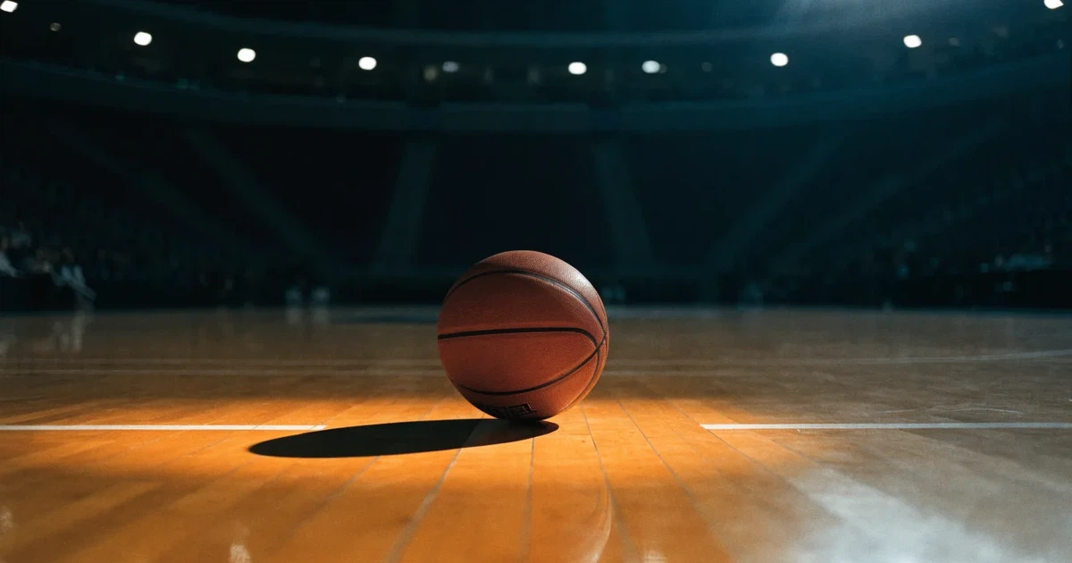 Ein orangefarbener Basketball liegt auf dem Parkett einer leeren Halle unter hellem Flutlicht, die Tribünen sind dunkel.