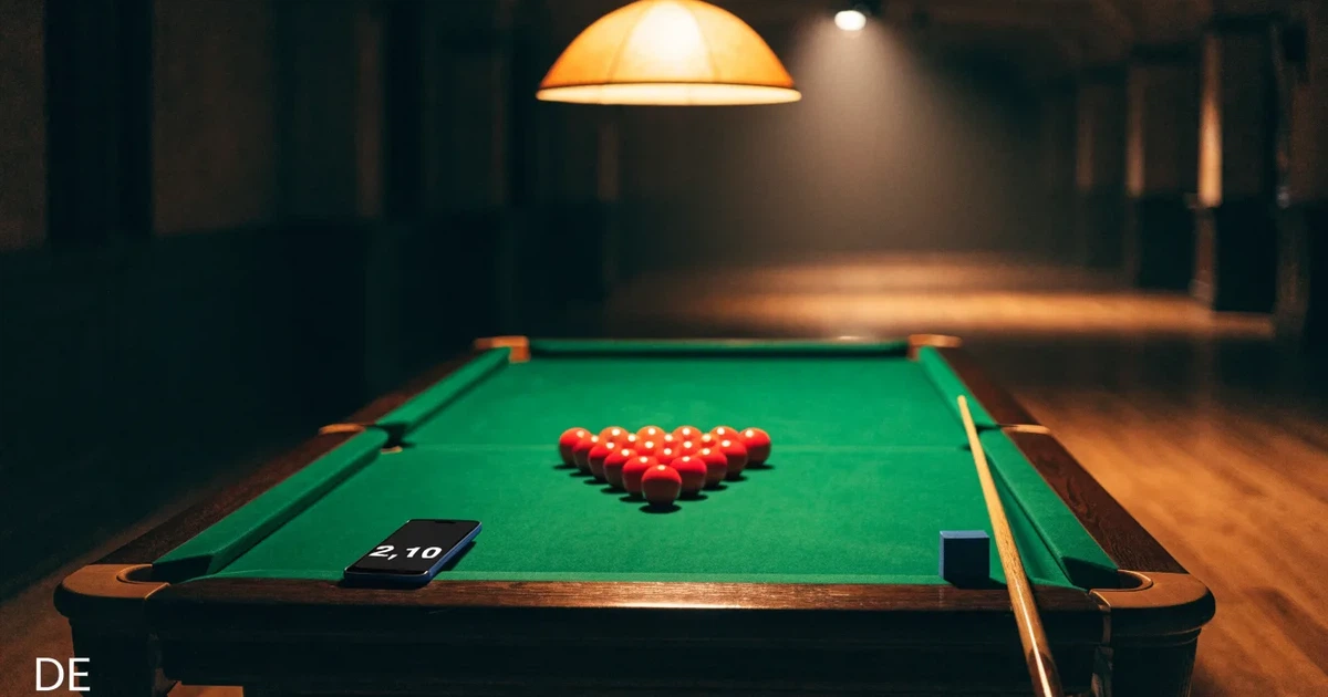 Ein Snookertisch mit grünem Tuch und einem Dreieck aus roten Kugeln unter einer tief hängenden Lampe in einer leeren Halle.
