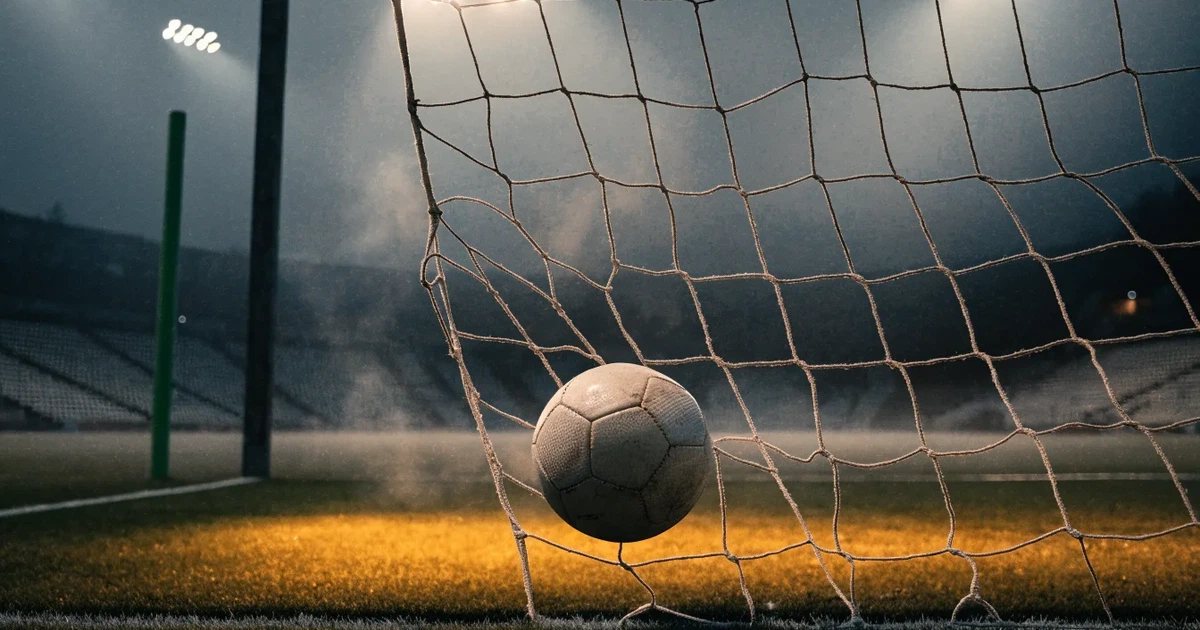 Ein Fussball liegt im Netz eines Tores, Flutlicht und kalte Abendluft liegen über dem leeren Platz